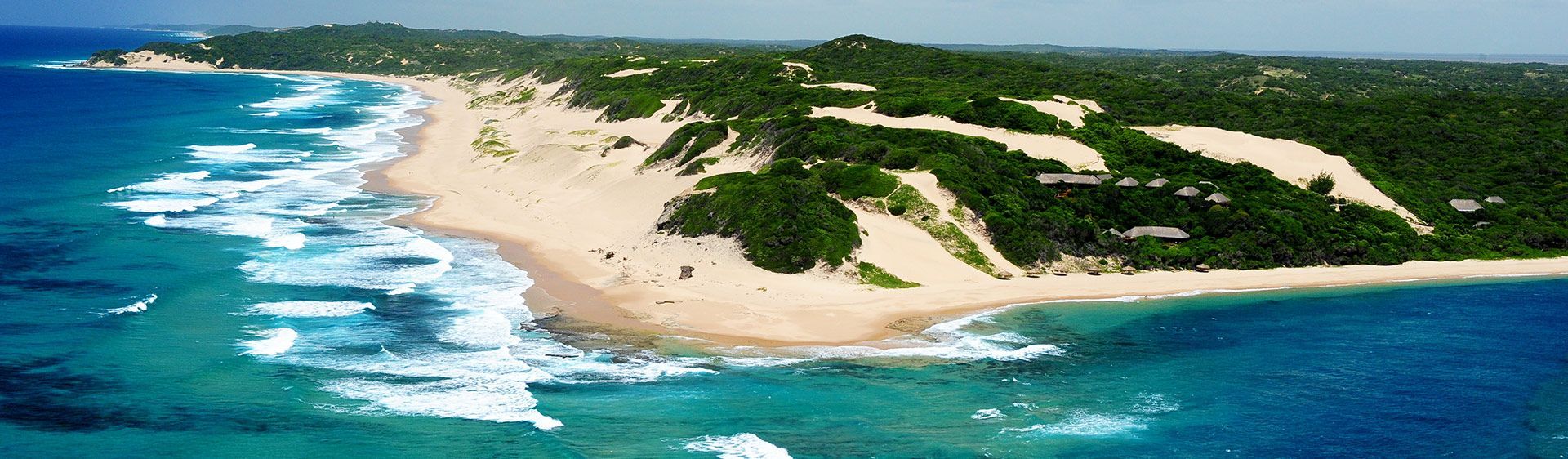 Aerial view of a sandy beach with turquoise waves and green dunes