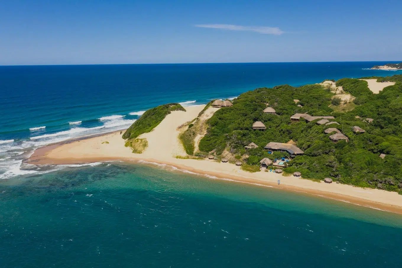 Aerial view of a tropical beach with turquoise water, sandy shore, and green coastal vegetation with huts