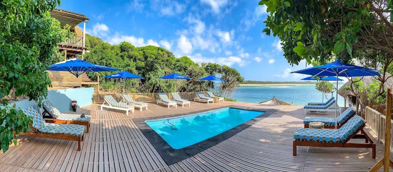 Tropical resort pool deck with blue loungers, umbrellas, and ocean views at sunset