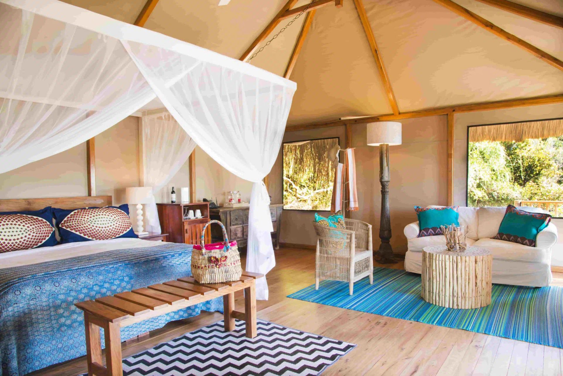Luxury safari tent bedroom with canopy bed, wooden table, woven chairs, and blue accent rugs