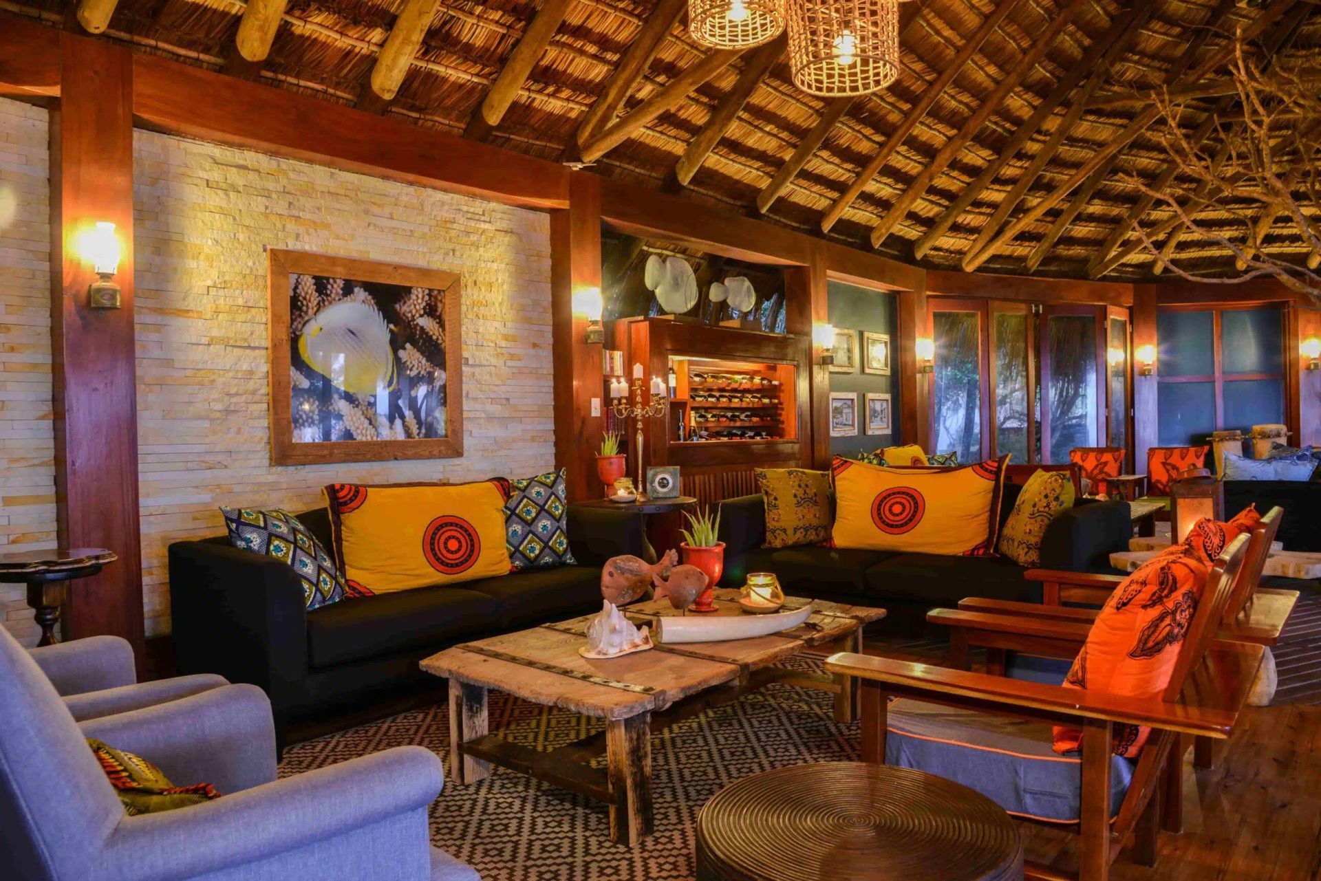 Cozy tropical lounge with woven ceiling, black sofas, orange cushions, and a wooden coffee table