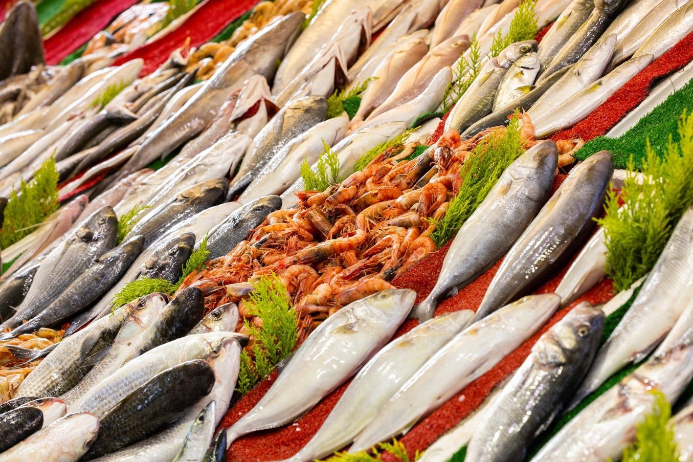 Fresh fish displayed on crushed ice at a market, with red chili garnish and green herbs