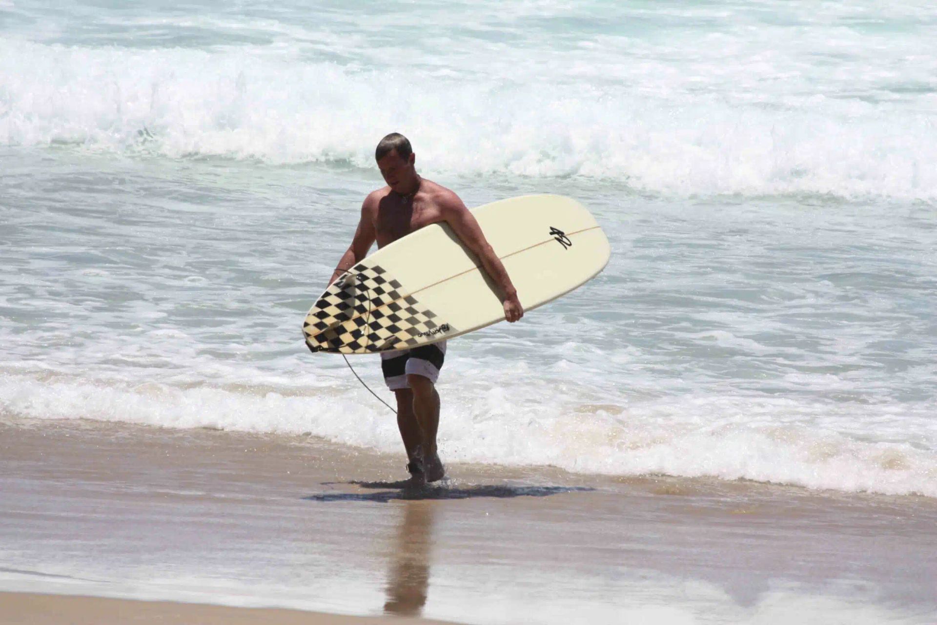 Surfer carrying a yellow surfboard at the shoreline with waves breaking in the background