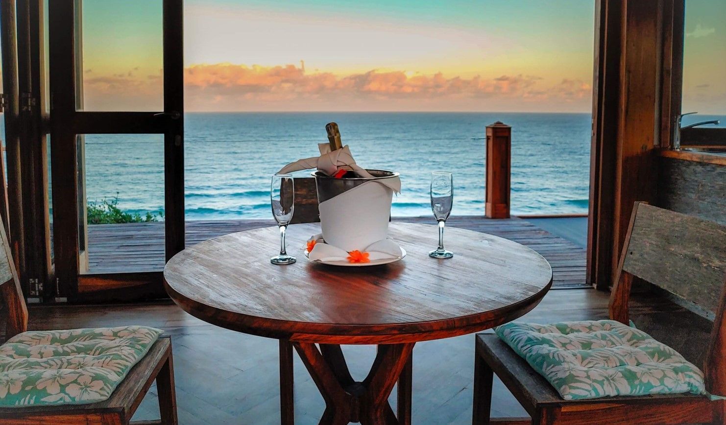 Cozy seaside table with a candle and wine cooler, framed by a window at sunset over the ocean