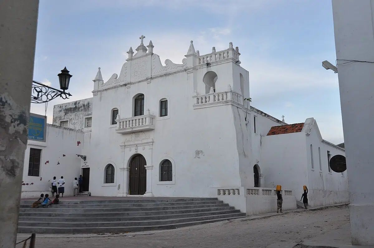 White historic church with ornate facade and steps in a quiet plaza under a blue sky