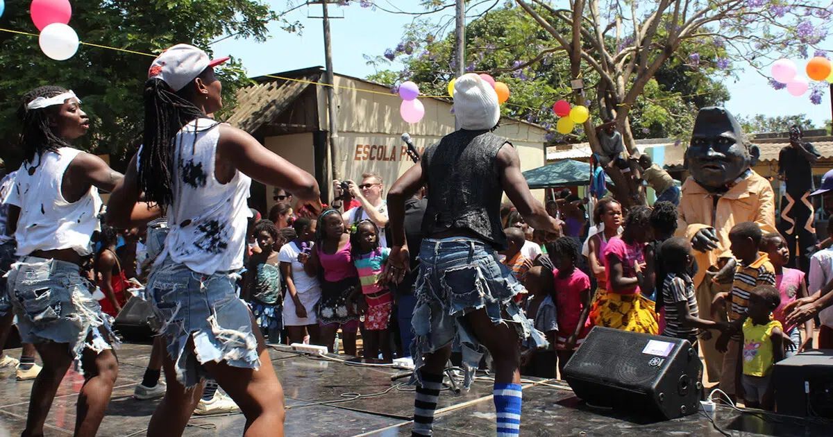 Dancers in denim performing outdoors on a stage for a crowd with balloons floating in the background.