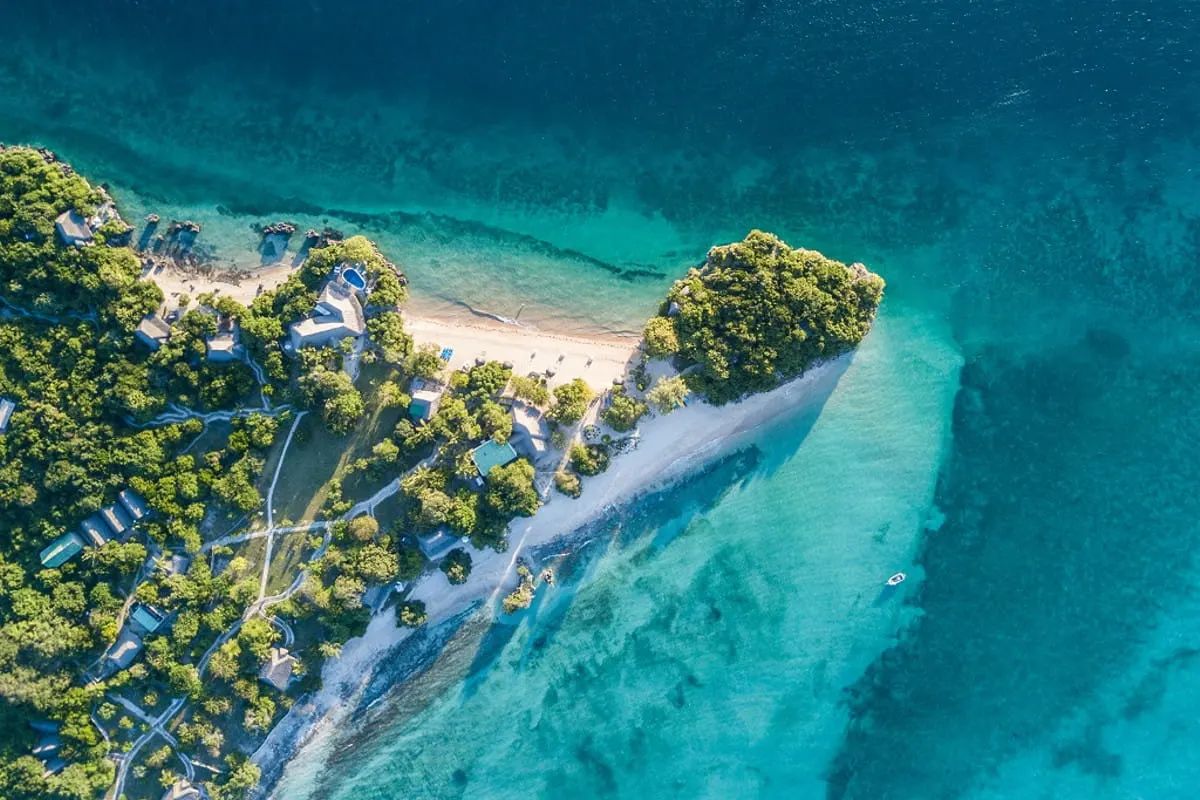 Aerial view of a forested peninsula with white sand beaches meeting turquoise and deep blue ocean water.