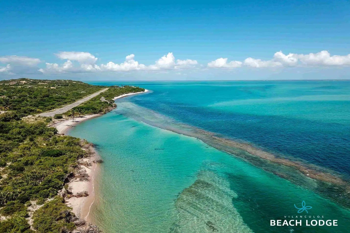 Aerial view of a turquoise coastal bay with green shoreline and a small beach lodge watermark