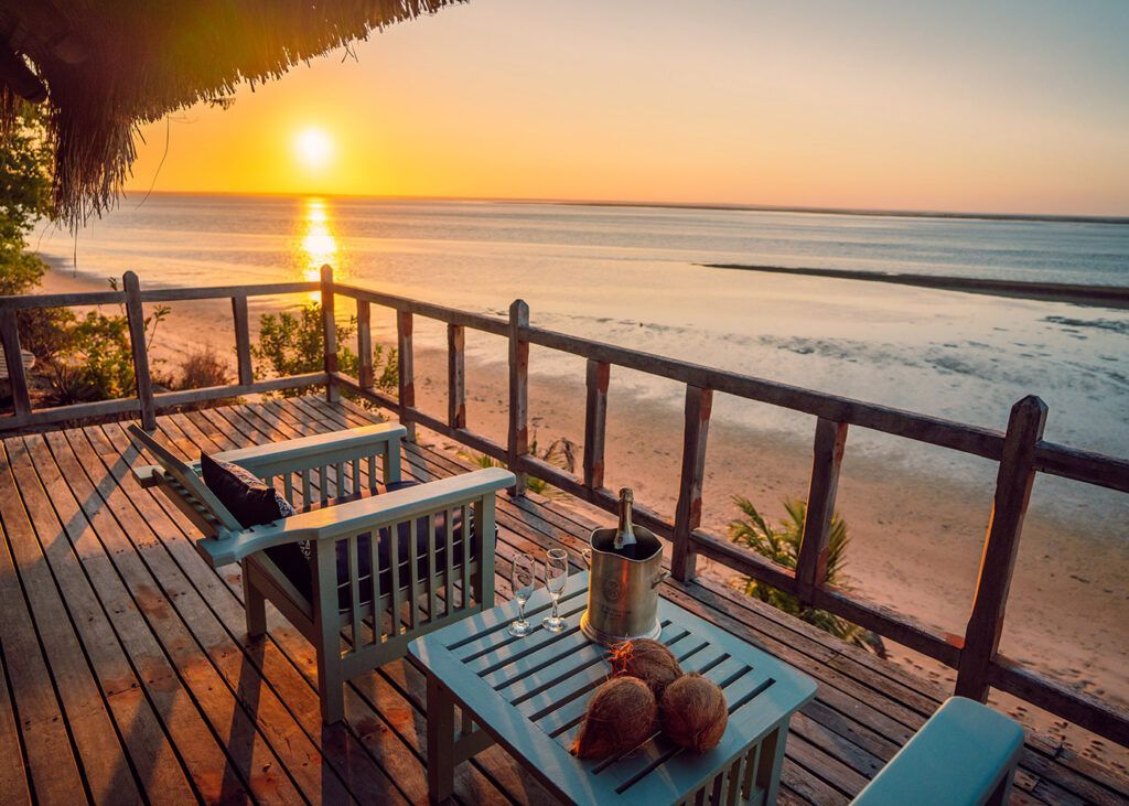 Sunset view from a wooden deck with table, chairs, and ocean beyond the railing