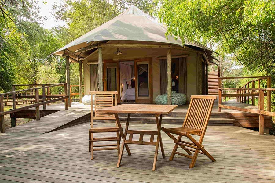 Wooden deck with table and chairs outside a round canvas cabin in a leafy forest setting