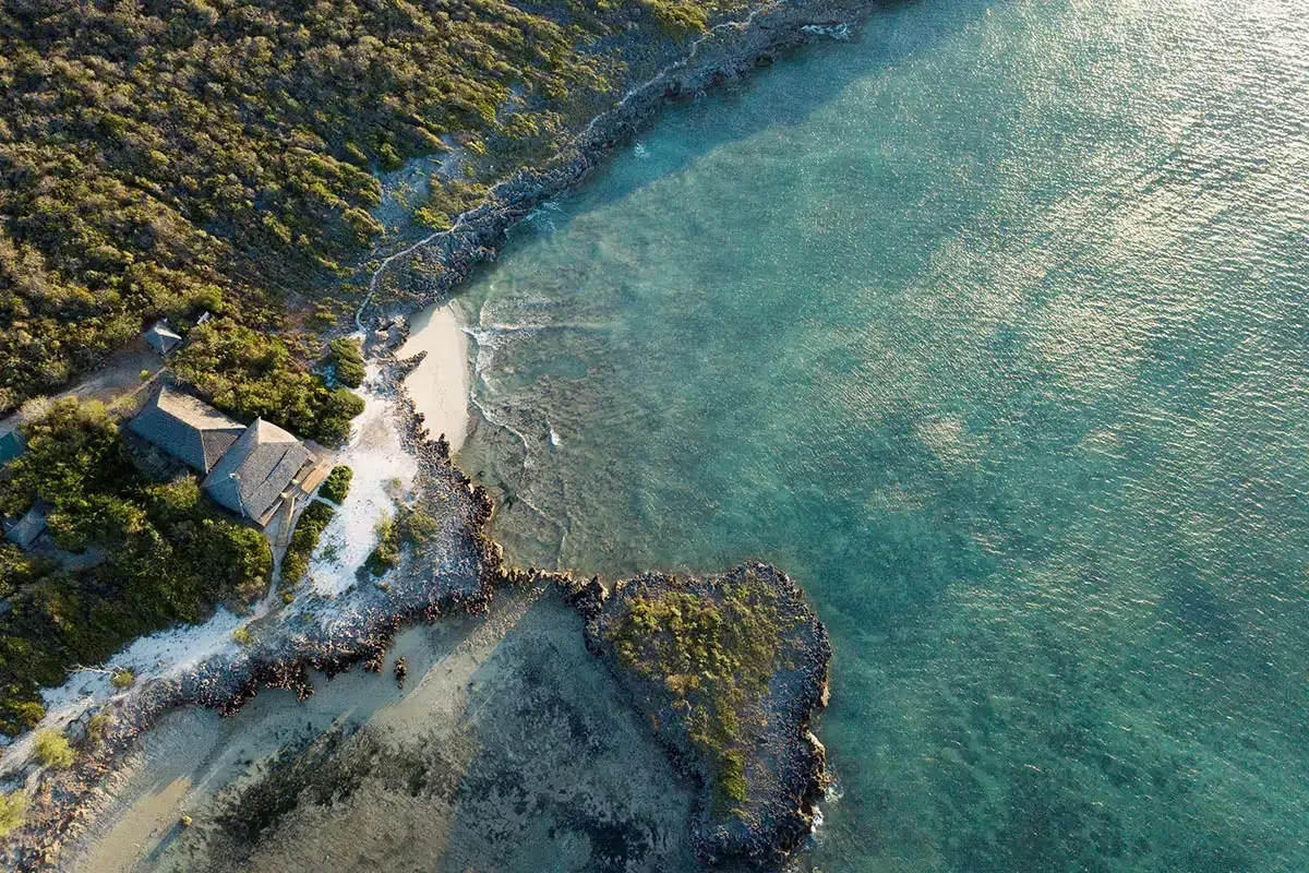 Palm-framed sandy beach with a turquoise lounge chair and calm ocean at sunset