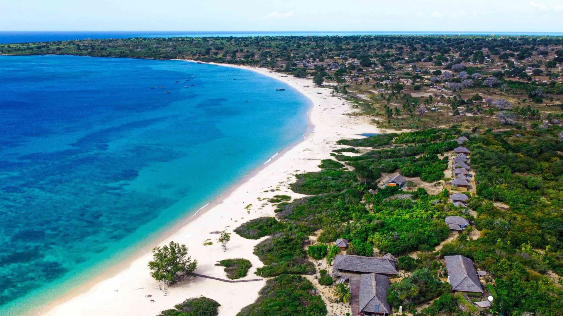 Aerial view of a turquoise beach with white sand and resort buildings along a lush coastline