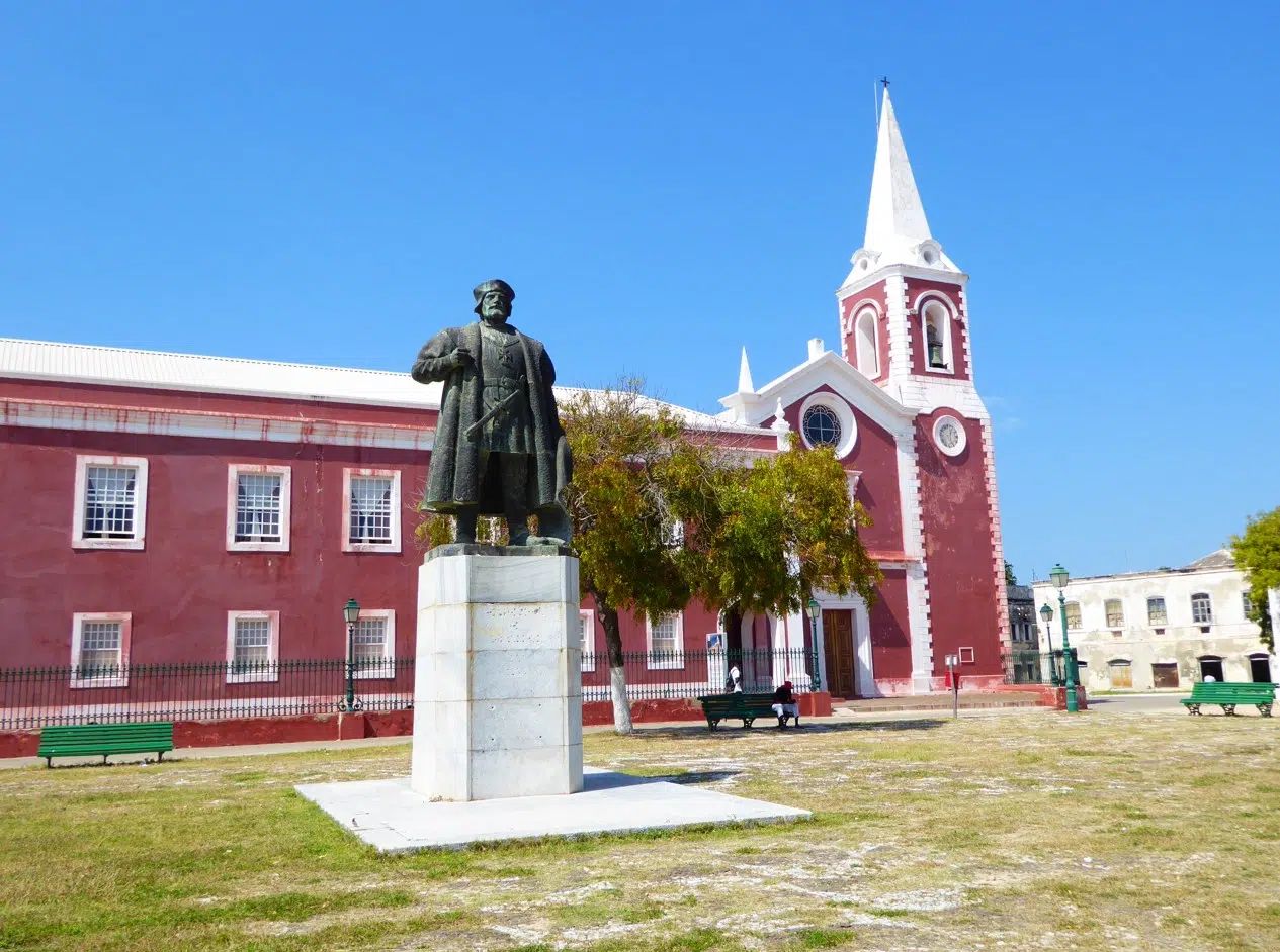 Statue in a plaza before a red church with a white steeple and surrounding buildings