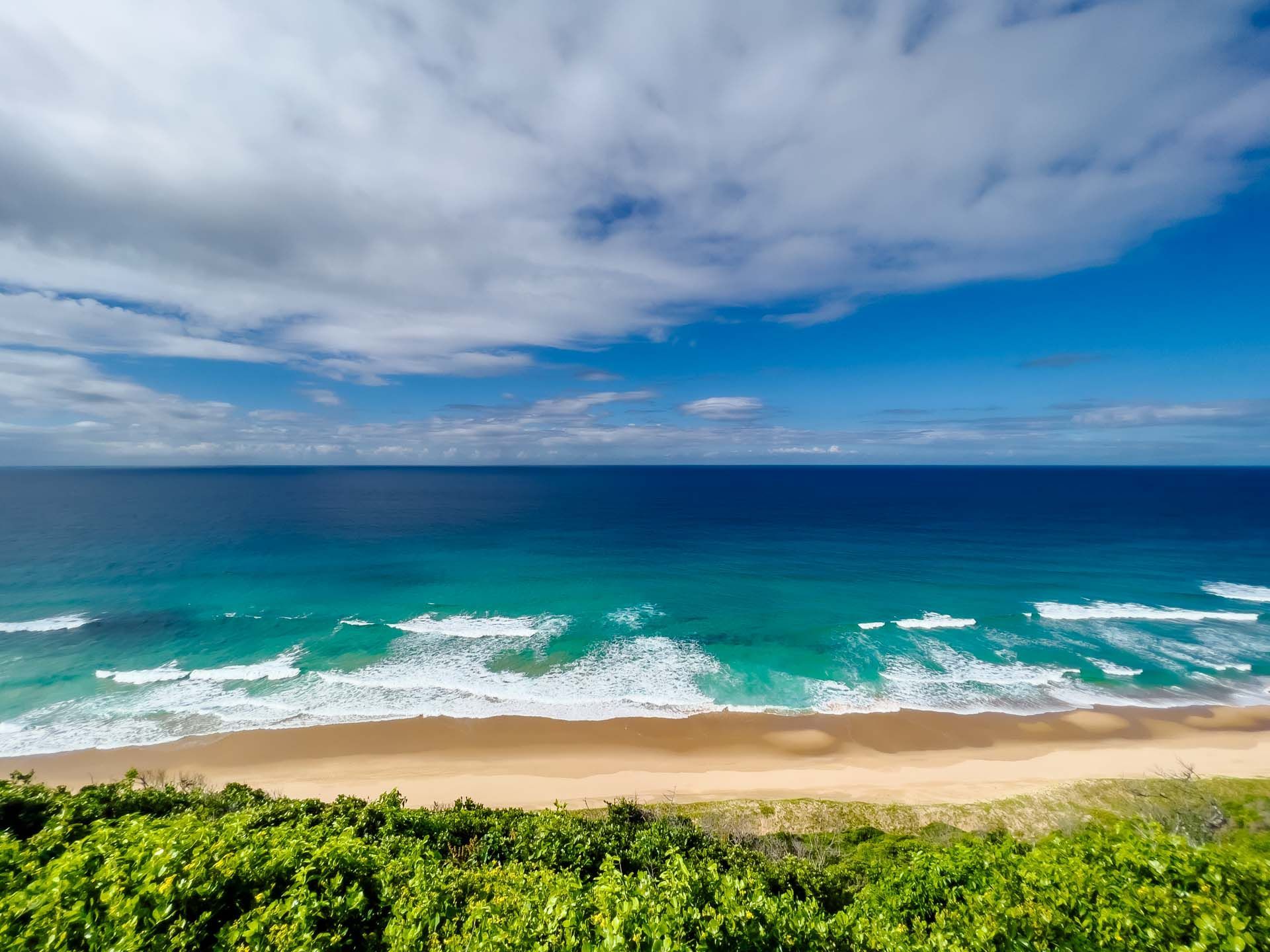 Tropical beach with turquoise waves, sandy shore, and a cloudy blue sky