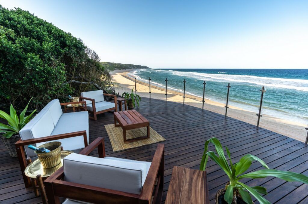 Beachfront deck with lounge chairs, tables, and umbrellas overlooking the ocean and shoreline
