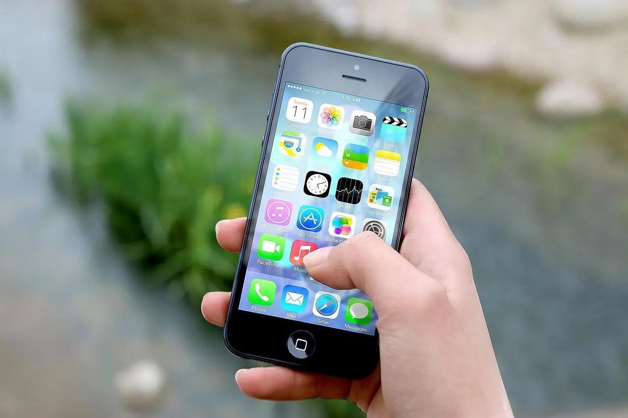 Hand holding a smartphone with app icons on the screen outdoors