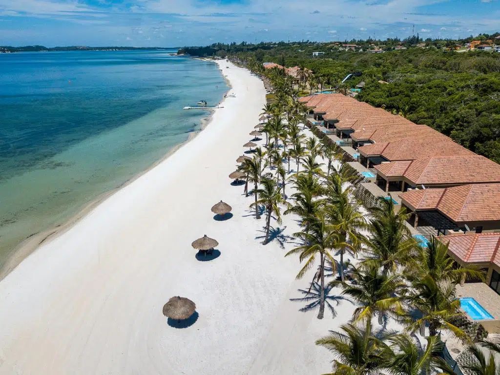 Aerial view of a tropical beach with white sand, turquoise water, palm trees, and seaside resort villas