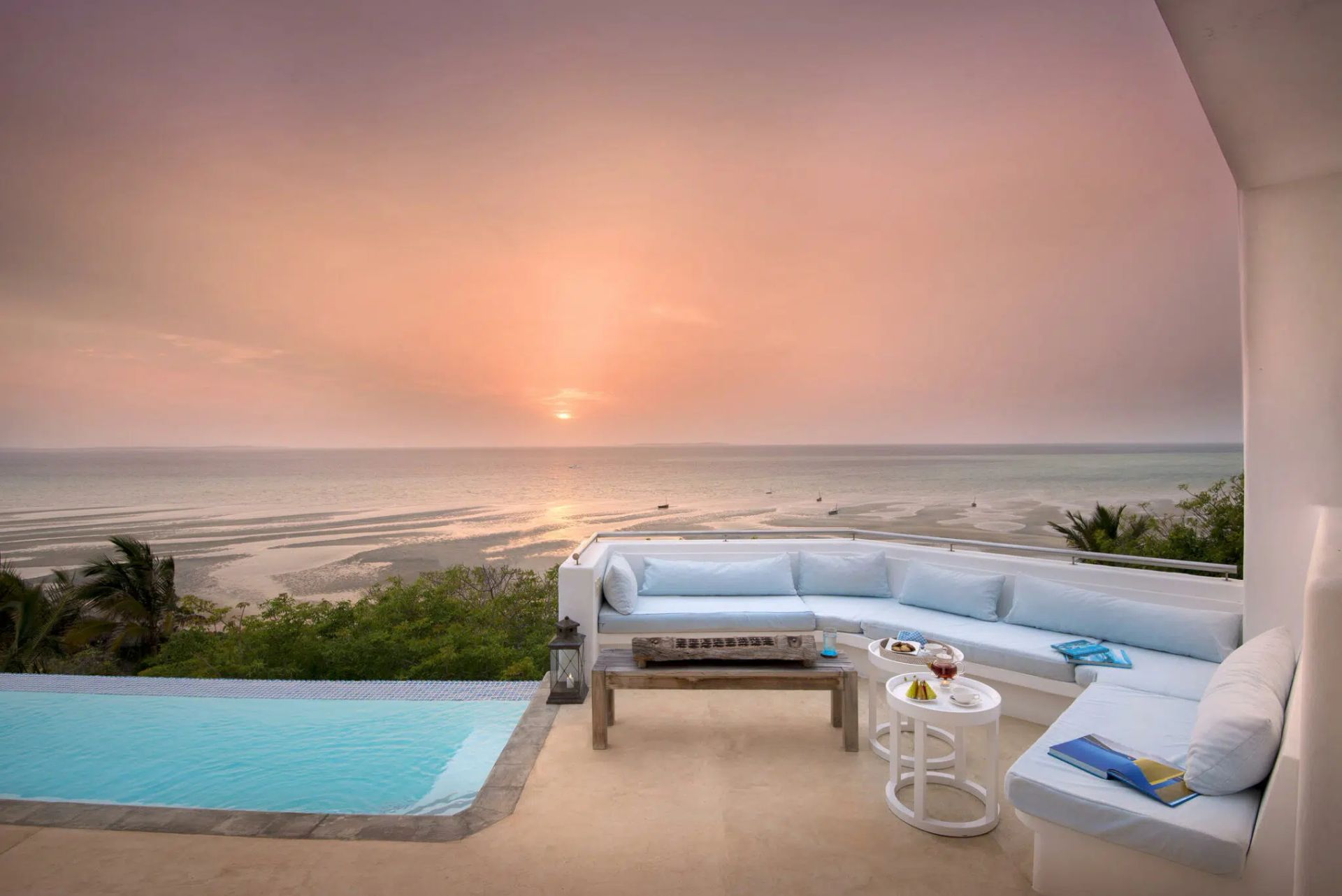 Sunset ocean view from a patio with white sectional seating and a turquoise pool