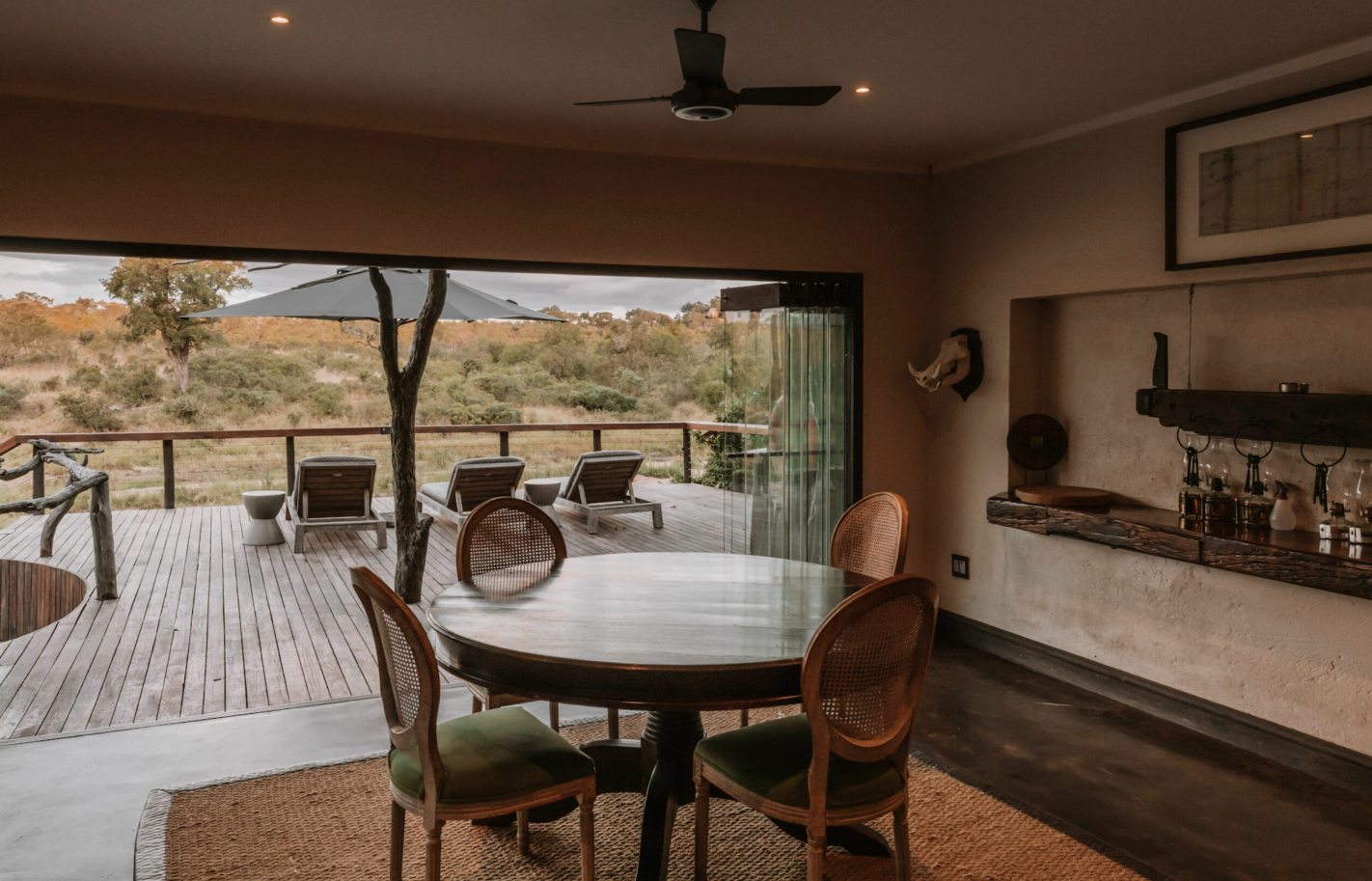Open patio dining area with round table, chairs, and desert view beyond the deck