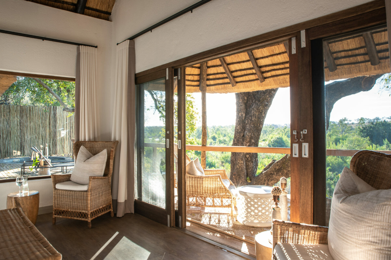 Sunlit living room with wicker chairs opening to a shaded balcony and green landscape beyond