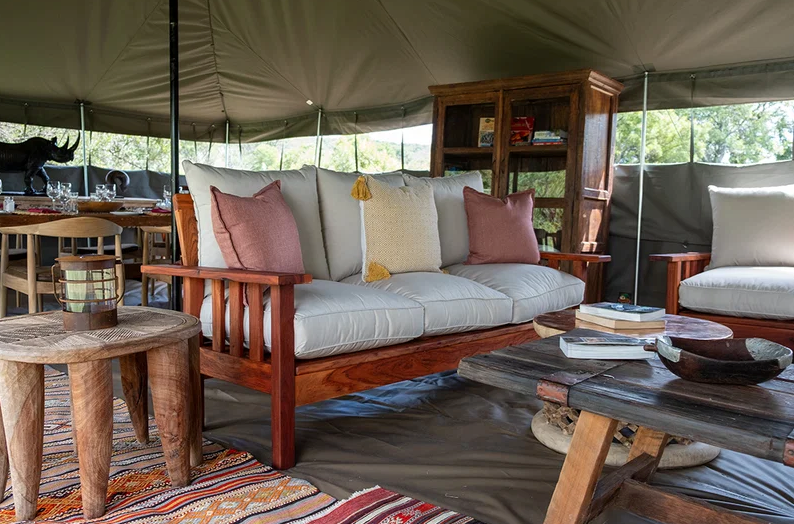 Cozy safari-style tent lounge with wooden sofas, coffee table, rugs, and cushions