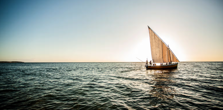 Small sailboat with tan sail on calm ocean at sunset