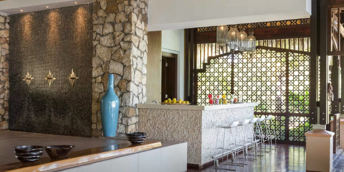 Modern lounge with stone wall, white tufted seating, patterned screen, and blue vase on a table