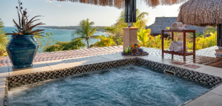 Shaded patio with a bubbling hot tub, potted plants, and an ocean view beyond the deck
