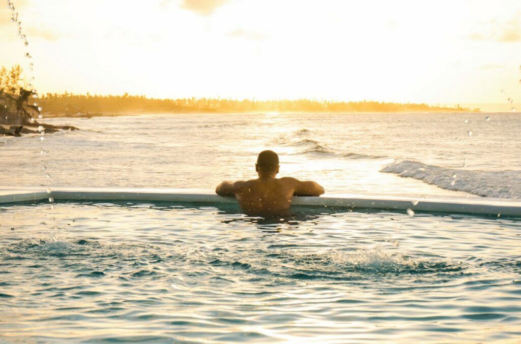 Person resting in a pool at sunset with ocean and glowing horizon in the background