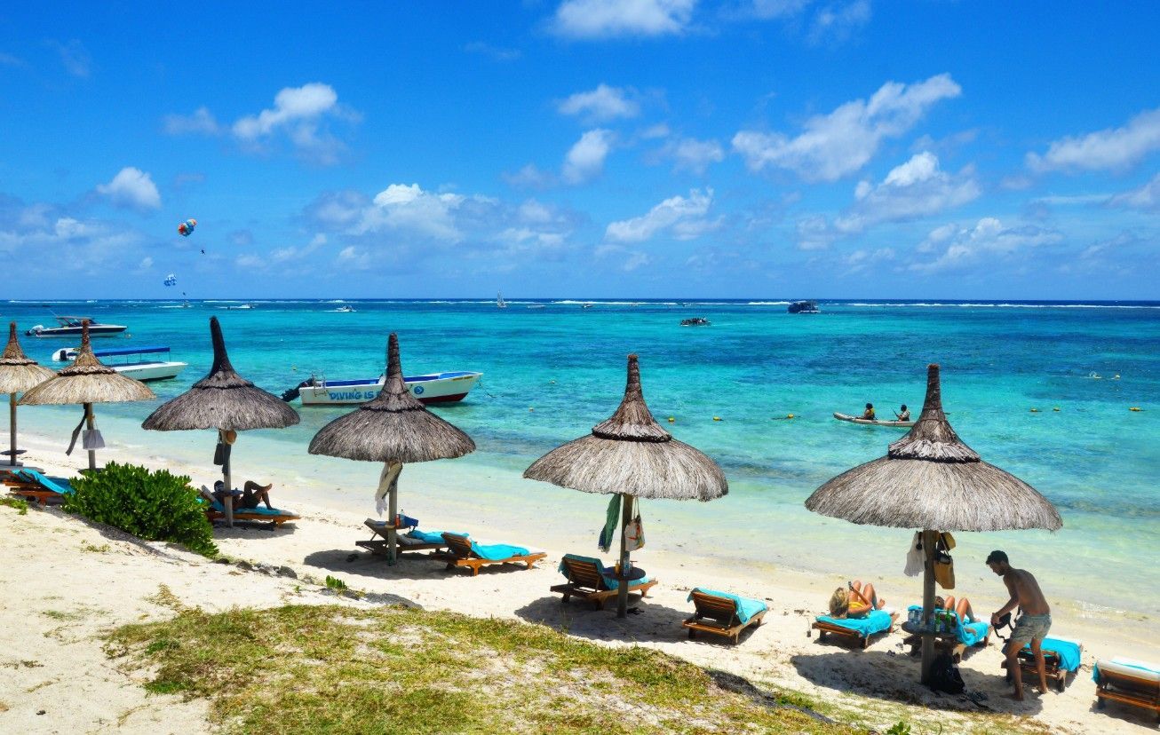 Sunny tropical beach with thatched umbrellas, lounge chairs, and turquoise ocean under a blue sky