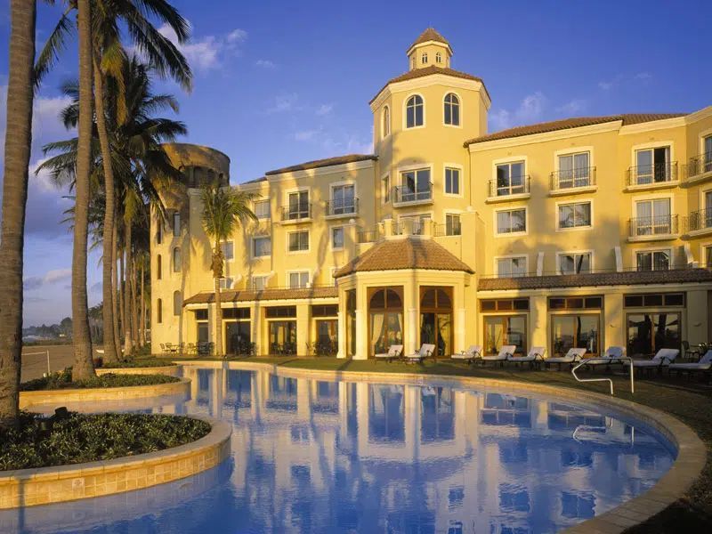 Yellow hotel with a curved pool and palm trees at sunset