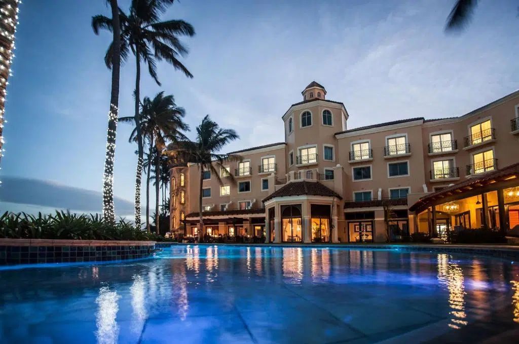 Luxury hotel pool at dusk with blue reflections and lit windows under a palm-lined sky