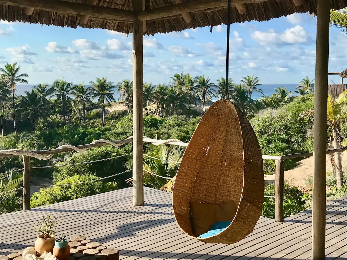 Tropical patio with a hanging egg chair overlooking lush palm trees and the ocean
