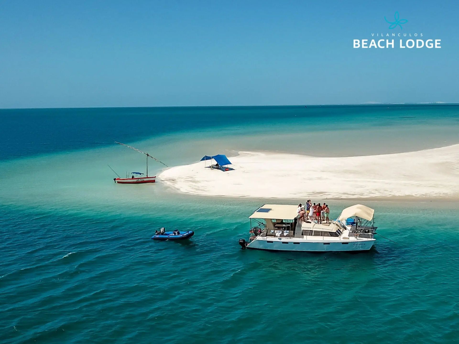 Turquoise sea with a sandy beach, small boat, and overwater beach lodge near shore.
