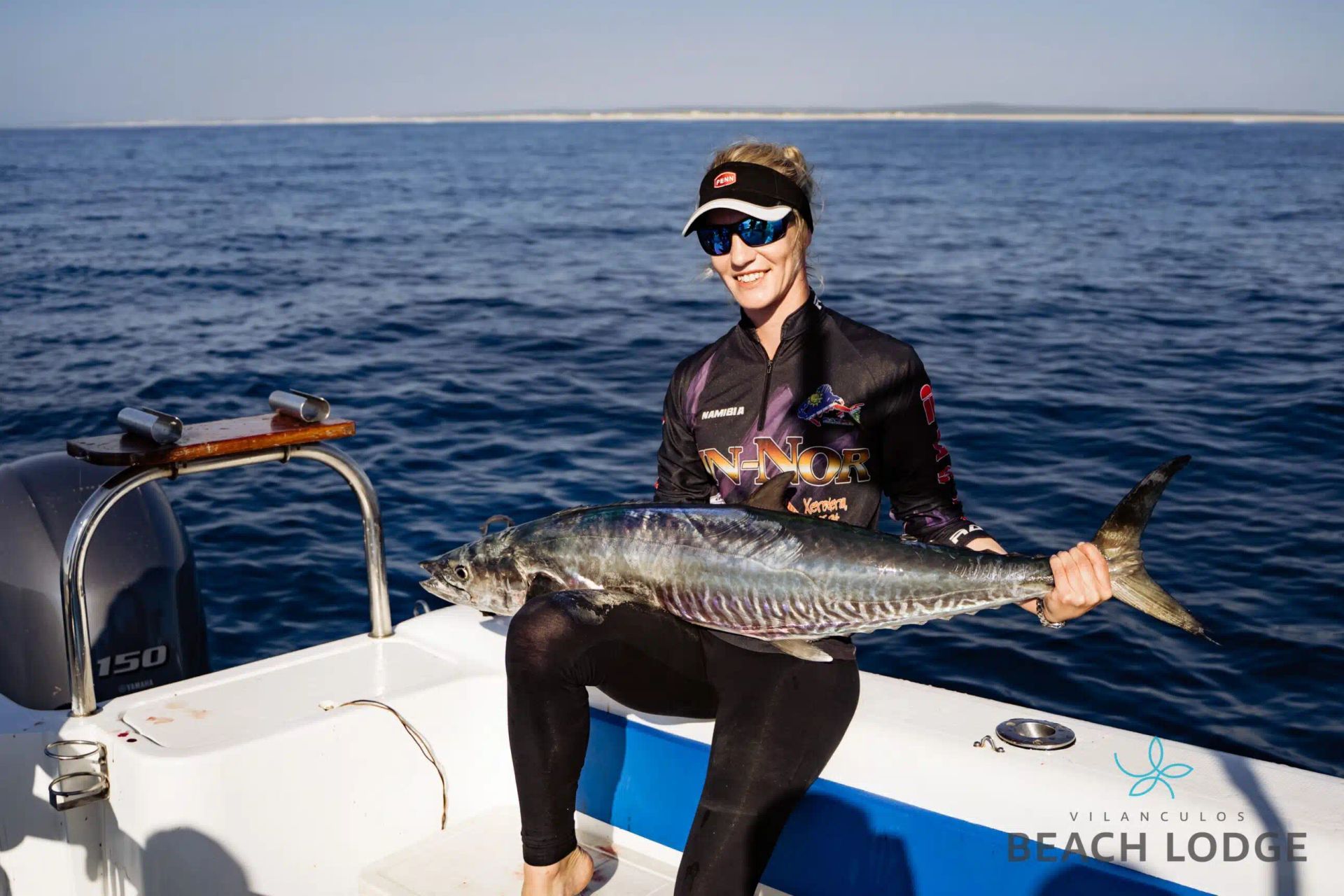 Person in sunglasses holds a large fish on a boat in open water.