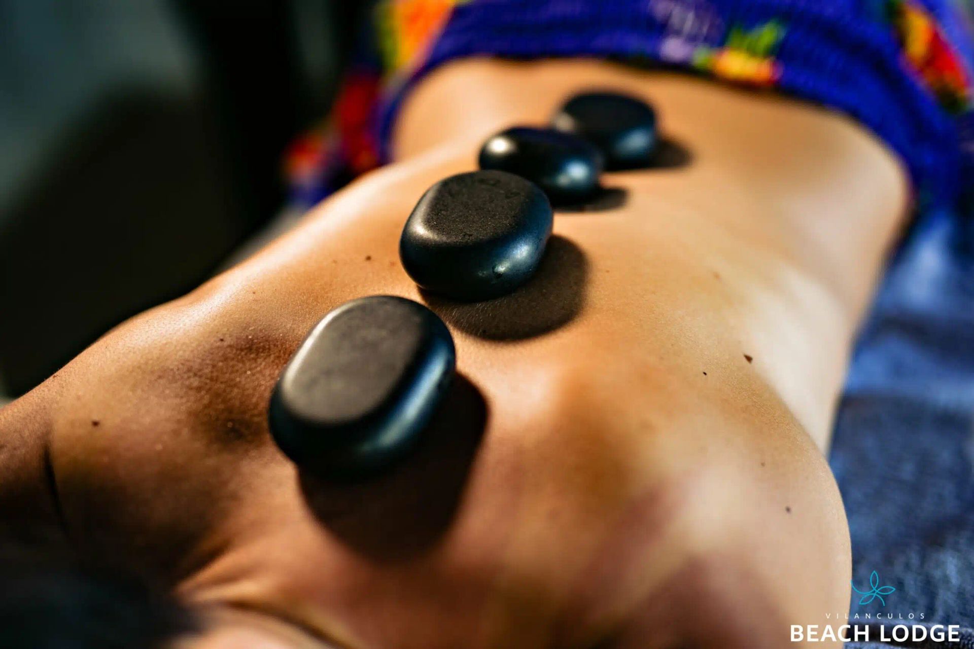A person lying face down receiving a hot stone massage, with smooth, dark stones placed along their spine.