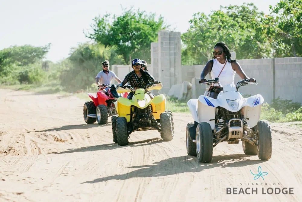Three people riding ATVs on sandy dunes near Beach Lodge