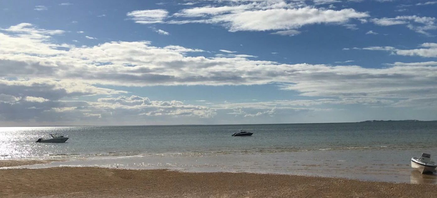 Sunny beach with calm sea, scattered clouds, and two small boats near shore