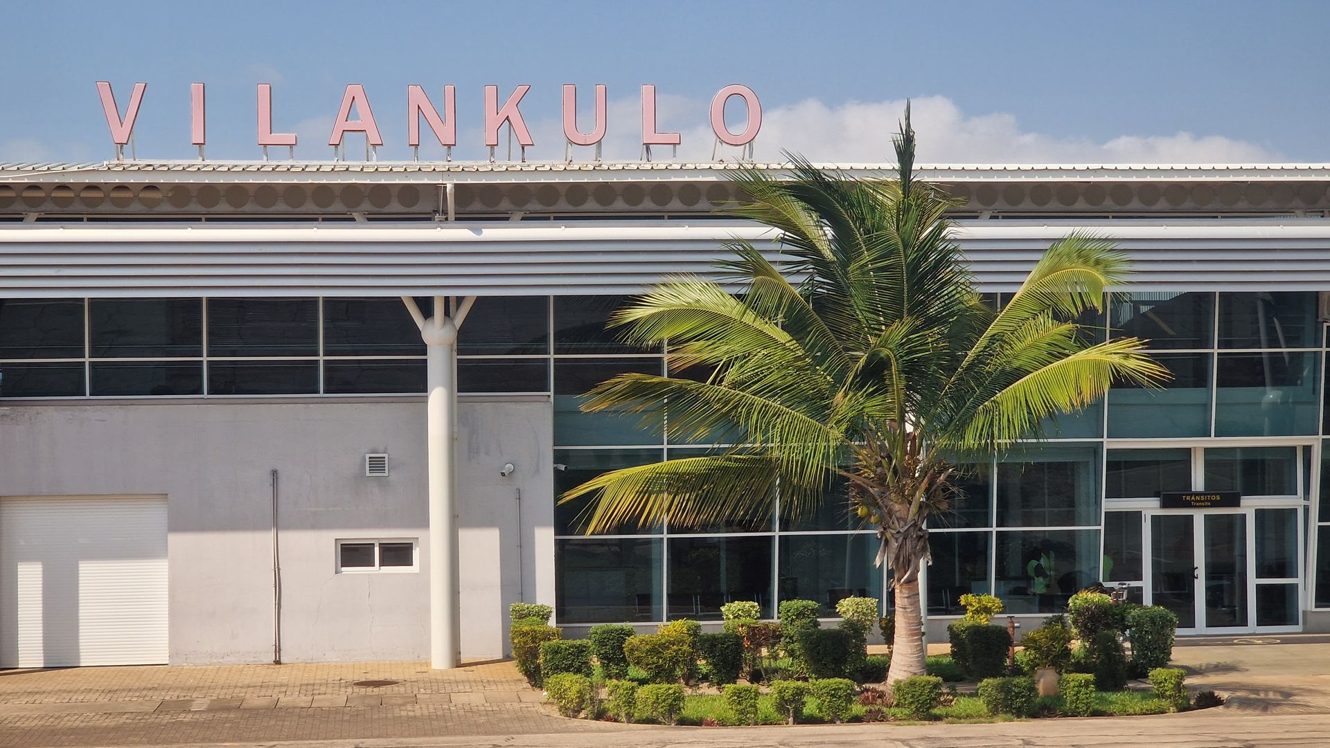 VILANKULO airport terminal with glass facade, palm tree, and clear sky