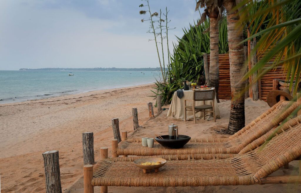 Palm-framed sandy beach with a turquoise lounge chair and calm ocean at sunset