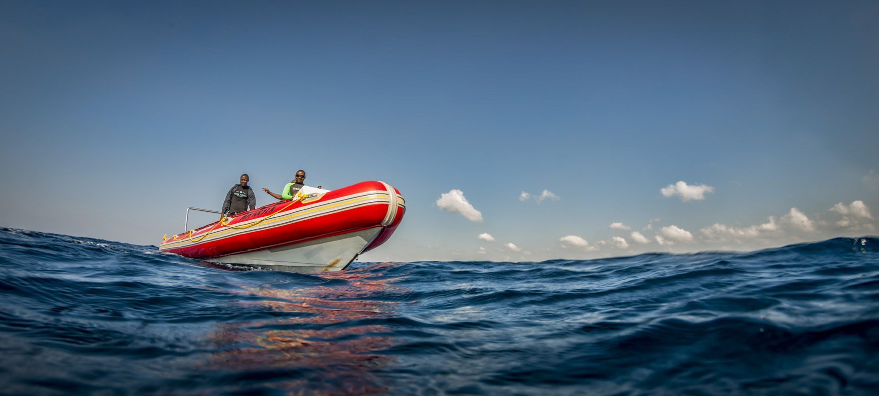 Red boat with two people skimming over rough blue ocean under a clear sky