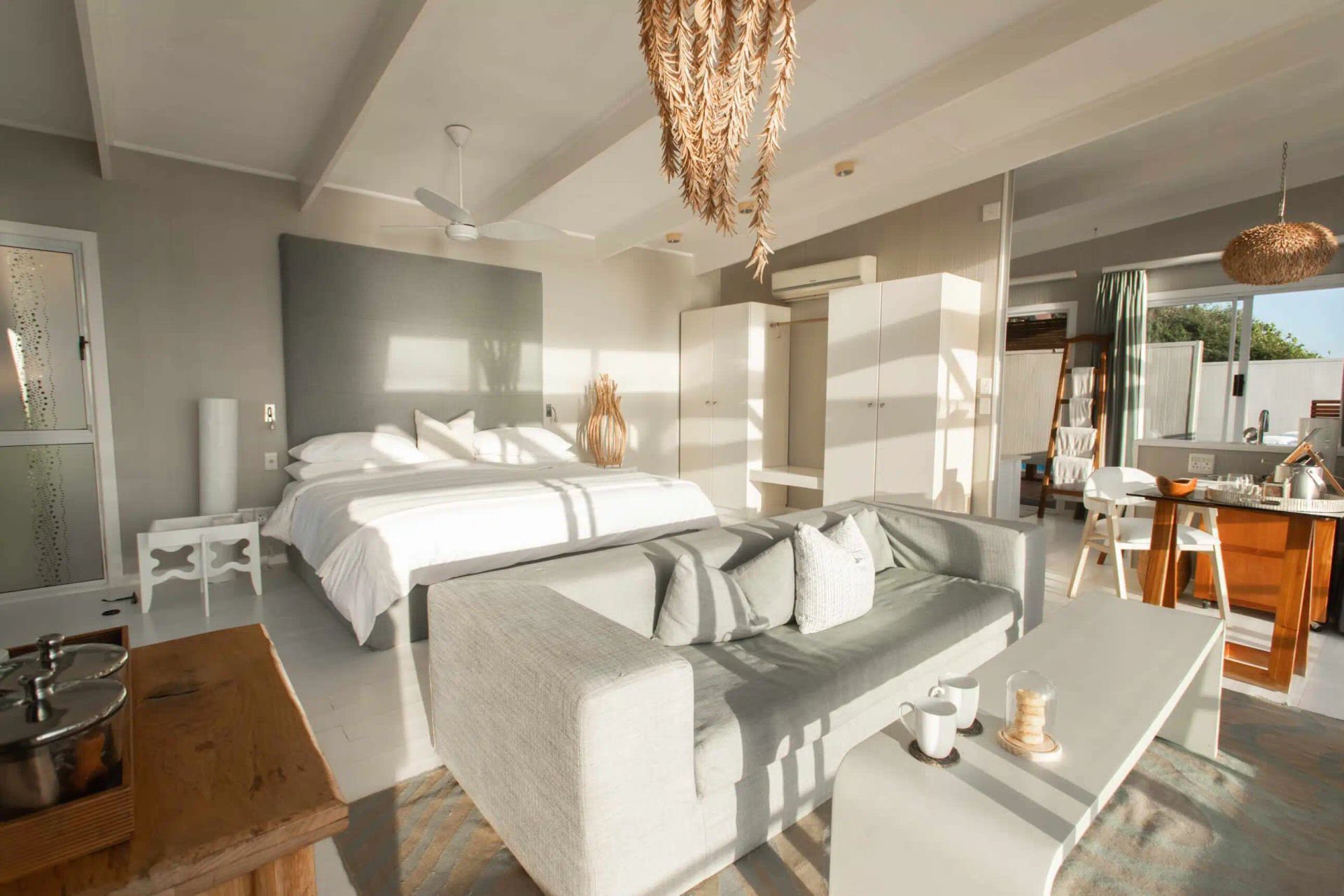 Bright modern bedroom with a bed, sofa, coffee table, and sunlit windows