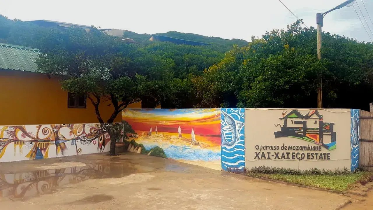 Colorful mural wall in a courtyard with trees, hills, and a sign for Xal-A Eco Estate.