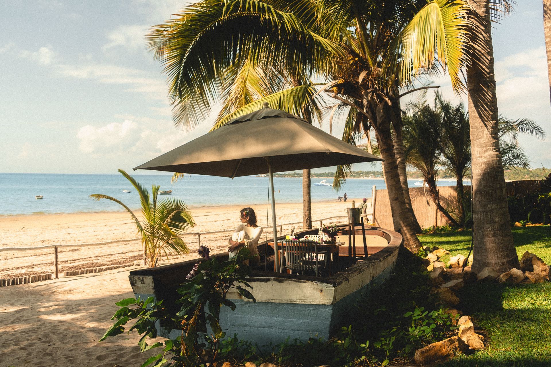 Tropical beachside patio with umbrella, palm trees, and ocean view at sunset