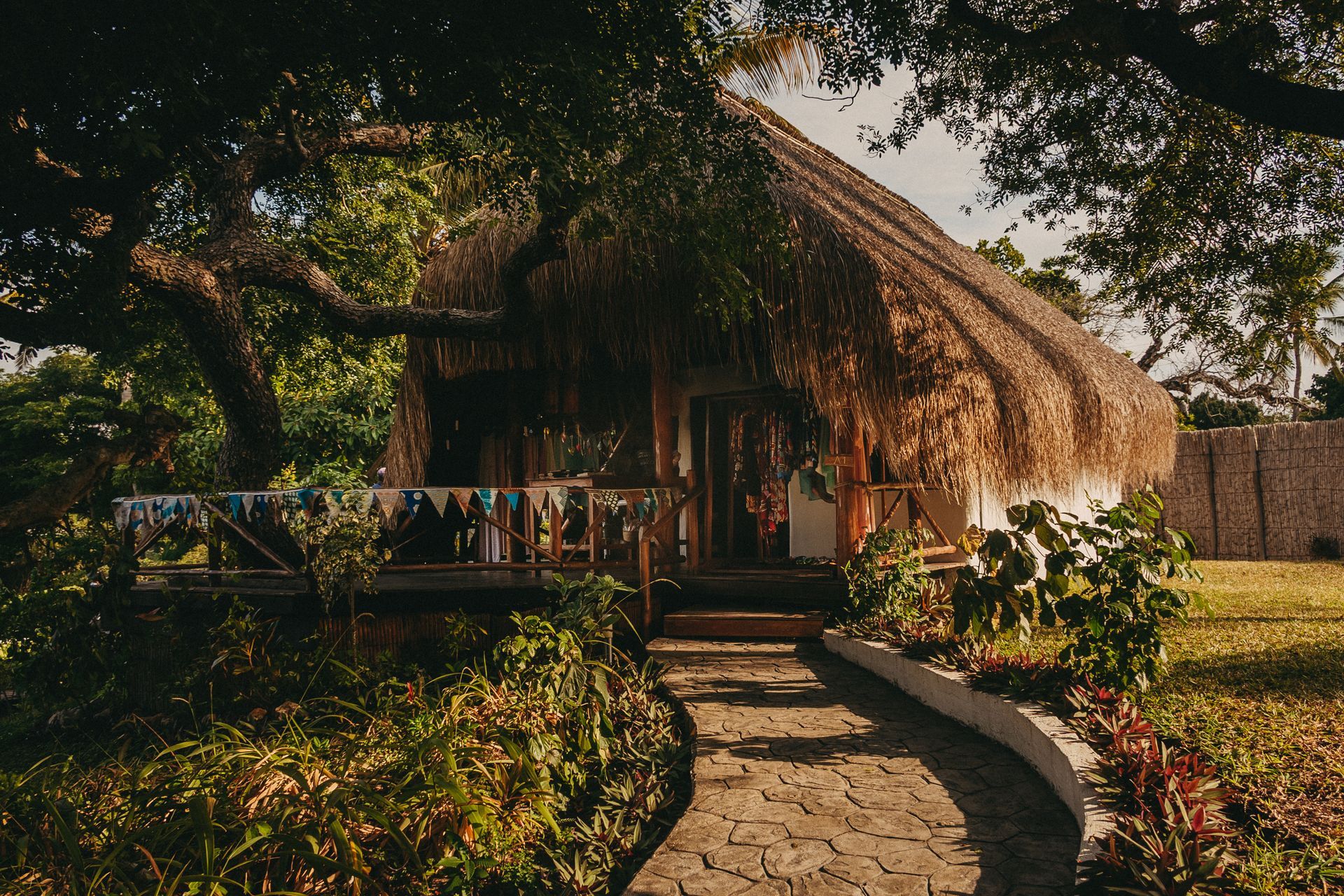 Thatched hut in a lush garden with a curved stone path and porch railing