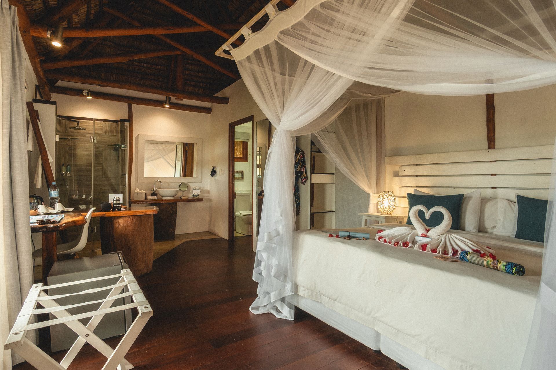 Bright bedroom with white canopy bed, wooden ceiling, and cozy seating area in rustic lodge style