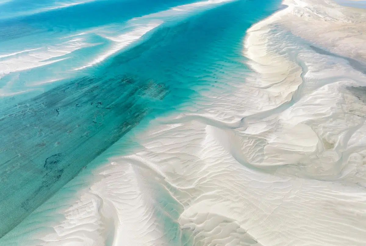 Turquoise tidal channel cutting through white sandbars in a coastal landscape
