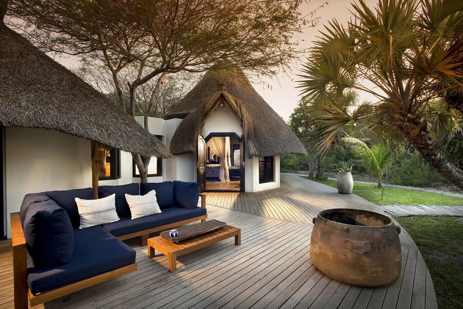 Thatched villa patio with navy sofa, wooden table, and fire pit among tropical trees