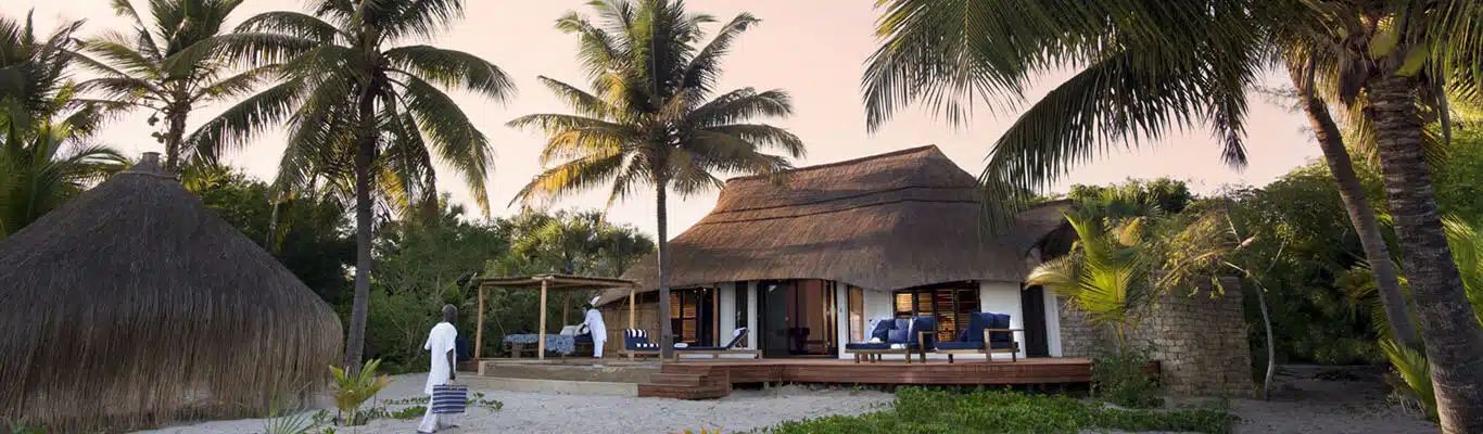 Thatched tropical resort building with palm trees and sandy path at sunset