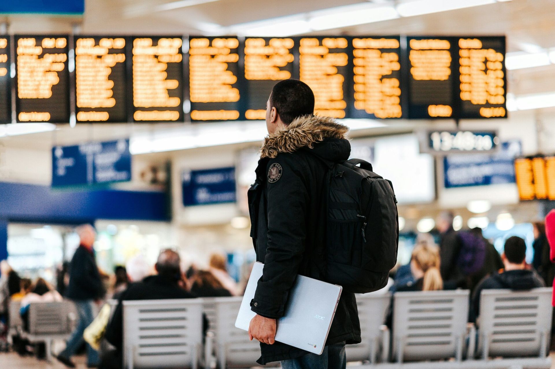 Traveler with backpack and papers stands in busy airport terminal beneath departure boards